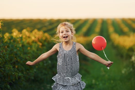 Positive little girl with red balloon in hands have fun on the field at summer day time photo