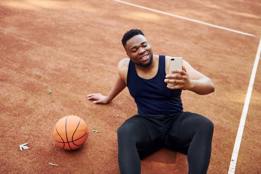 Making selfie. African american man plays basketball on the court outdoors photo
