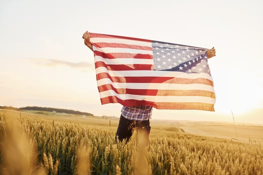 Holding USA flag in hands. Patriotic senior stylish man with grey hair and beard on the agricultural field photo