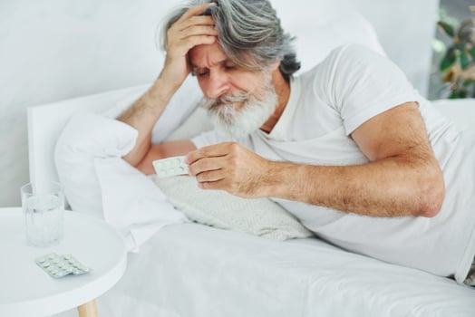 Sick senior stylish modern man with grey hair and beard indoors lying on the bed and feels bad photo