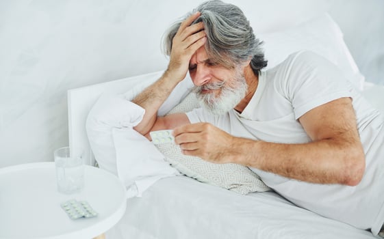Sick senior stylish modern man with grey hair and beard indoors lying on the bed and feels bad photo