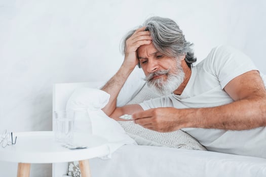 Sick senior stylish modern man with grey hair and beard indoors lying on the bed and feels bad photo
