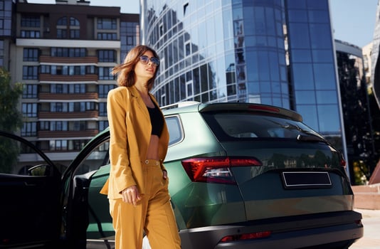 Walks forward from automobile. Young fashionable woman in burgundy colored coat at daytime with her car photo