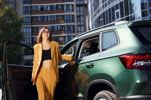 Walks forward from automobile. Young fashionable woman in burgundy colored coat at daytime with her car photo