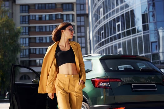 Walks forward from automobile. Young fashionable woman in burgundy colored coat at daytime with her car photo