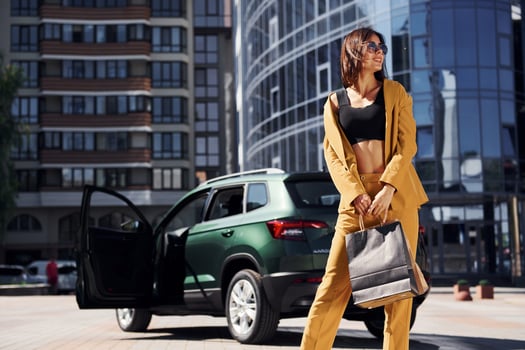 Modern business building at background. Young fashionable woman in burgundy colored coat at daytime with her car photo