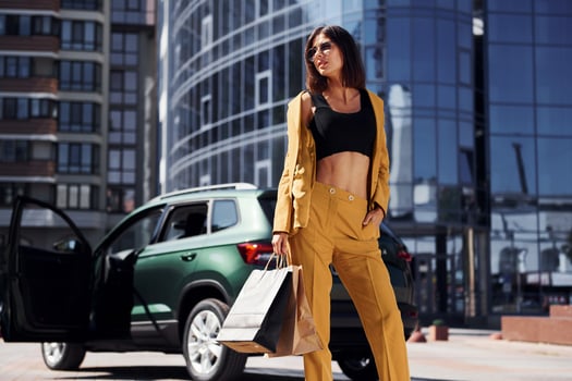 Modern business building at background. Young fashionable woman in burgundy colored coat at daytime with her car photo