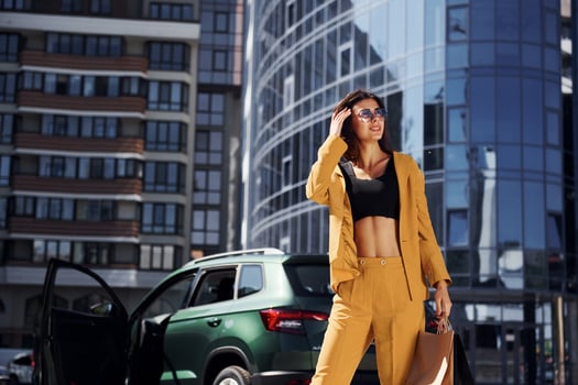 Modern business building at background. Young fashionable woman in burgundy colored coat at daytime with her car photo
