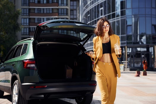 Modern business building at background. Young fashionable woman in burgundy colored coat at daytime with her car photo