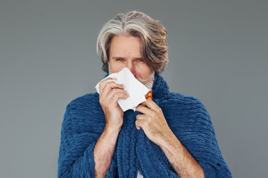 Getting sick. Against grey background. Stylish modern senior man with gray hair and beard is indoors photo