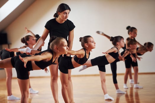 Coach is helping. Group of female kids practicing athletic exercises together indoors photo