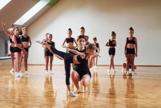 With help from coach. Group of female kids practicing athletic exercises together indoors photo