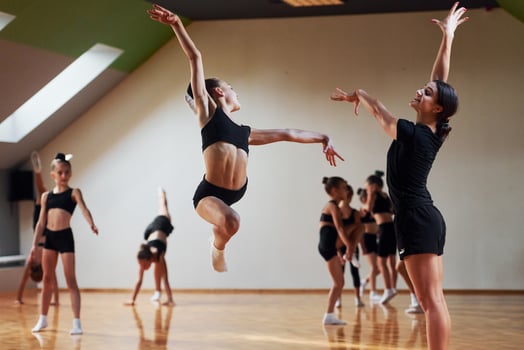 Woman teaching and helping. Group of female kids practicing athletic exercises together indoors photo