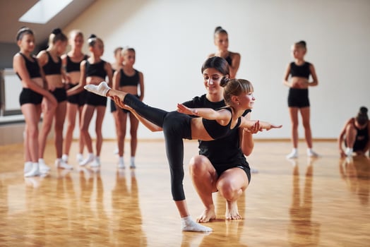 Woman teaching and helping. Group of female kids practicing athletic exercises together indoors photo