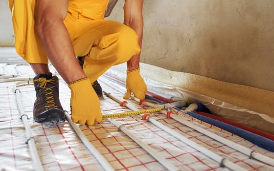 Measuring distance of the pipes. Worker in yellow colored uniform installing underfloor heating system photo