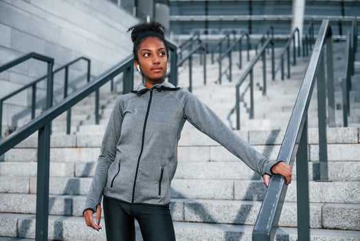 Listens to music in headphones. Young african american woman in sportive clothes have workout outdoors at daytime photo