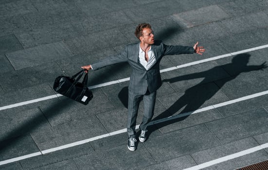 Dancing, celebrating success. Young businessman in grey formal wear is outdoors in the city photo