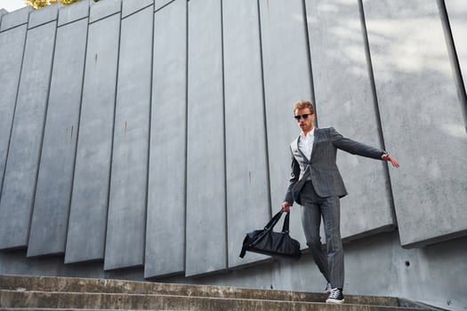 Dancing, celebrating success. Young businessman in grey formal wear is outdoors in the city photo