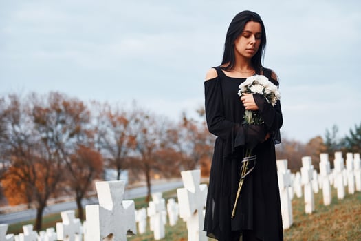 With flowers in hands. Young woman in black clothes visiting cemetery with many white crosses. Conception of funeral and death photo