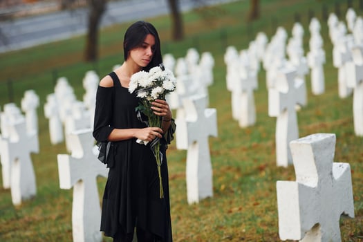 With flowers in hands. Young woman in black clothes visiting cemetery with many white crosses. Conception of funeral and death photo