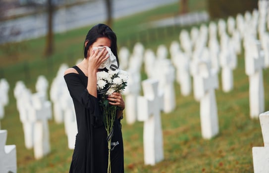 Young woman in black clothes visiting cemetery with many white crosses. Conception of funeral and death photo