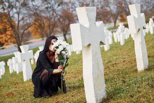 With flowers in hands. Young woman in black clothes visiting cemetery with many white crosses. Conception of funeral and death photo