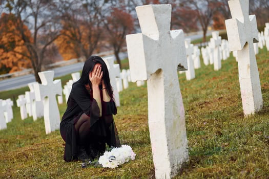 With flowers in hands. Young woman in black clothes visiting cemetery with many white crosses. Conception of funeral and death photo