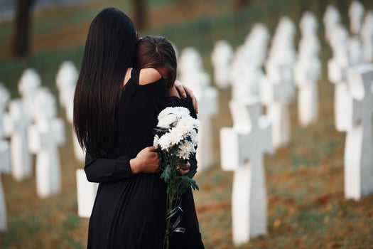 Embracing each other and crying. Two young women in black clothes visiting cemetery with many white crosses. Conception of funeral and death photo