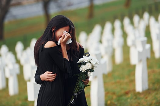 Embracing each other and crying. Two young women in black clothes visiting cemetery with many white crosses. Conception of funeral and death photo
