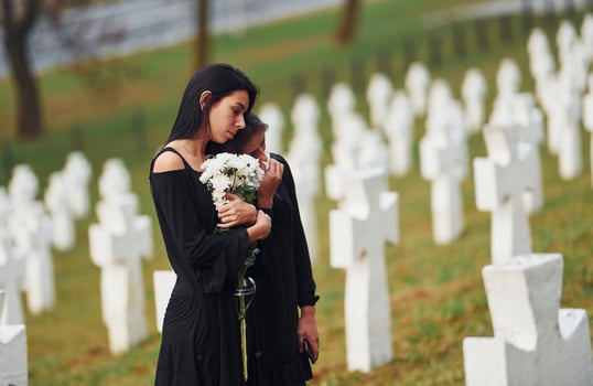 Holds flowers. Two young women in black clothes visiting cemetery with many white crosses. Conception of funeral and death photo