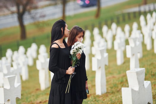 Holds flowers. Two young women in black clothes visiting cemetery with many white crosses. Conception of funeral and death photo