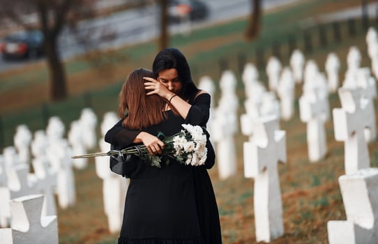 Embracing each other and crying. Two young women in black clothes visiting cemetery with many white crosses. Conception of funeral and death photo