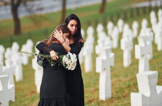 Embracing each other and crying. Two young women in black clothes visiting cemetery with many white crosses. Conception of funeral and death photo