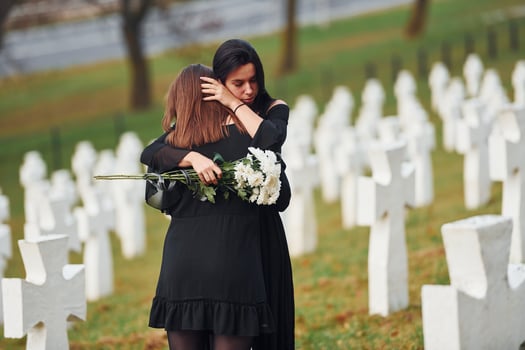 Embracing each other and crying. Two young women in black clothes visiting cemetery with many white crosses. Conception of funeral and death photo