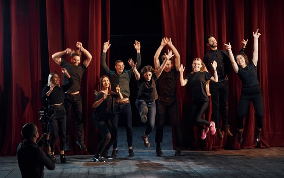 Happy people celebrating success. Group of actors in dark colored clothes on rehearsal in the theater photo