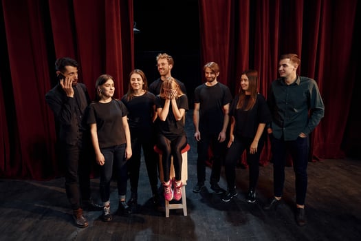 Girls sits on chair and crying. Group of actors in dark colored clothes on rehearsal in the theater photo