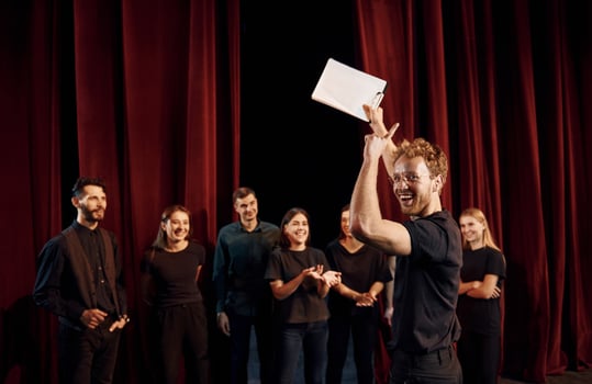 Man with notepad practice his role. Group of actors in dark colored clothes on rehearsal in the theater photo
