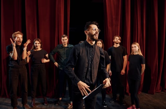 Expressionalible guy practicing his role. Group of actors in dark colored clothes on rehearsal in the theater photo