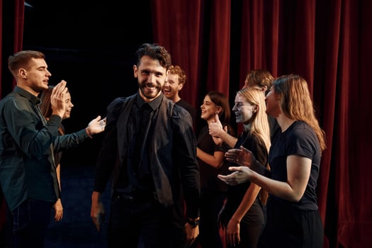 Giving high five, celebrating success. Group of actors in dark colored clothes on rehearsal in the theater photo