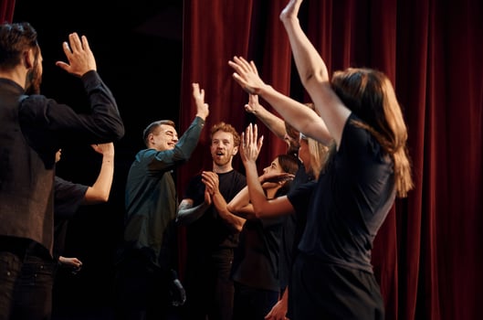 Giving high five, celebrating success. Group of actors in dark colored clothes on rehearsal in the theater photo