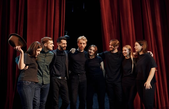 Standing against red curtains. Group of actors in dark colored clothes on rehearsal in the theater photo