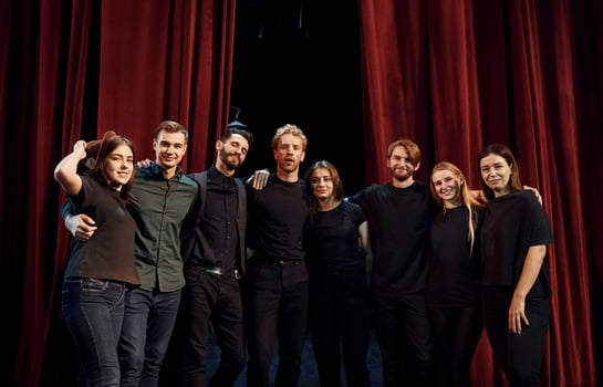 Standing against red curtains. Group of actors in dark colored clothes on rehearsal in the theater photo