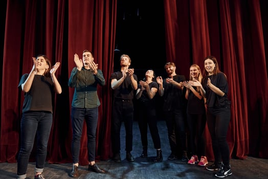 Standing against red curtains. Group of actors in dark colored clothes on rehearsal in the theater photo