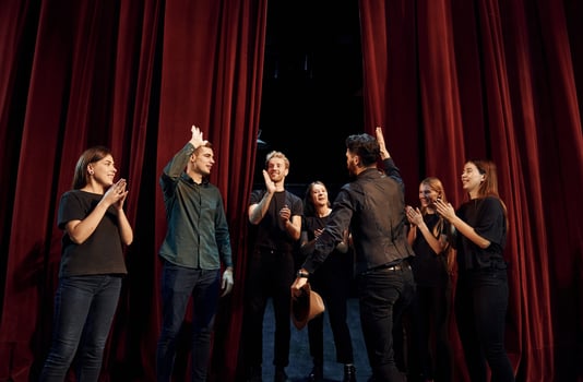 Standing against red curtains. Group of actors in dark colored clothes on rehearsal in the theater photo