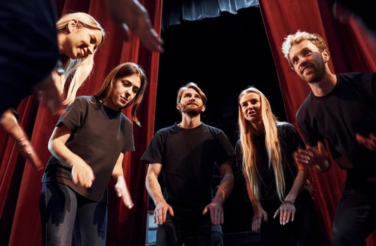 Standing against red curtains. Group of actors in dark colored clothes on rehearsal in the theater photo