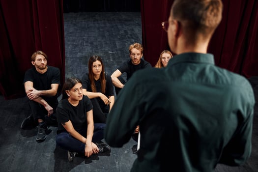 Sitting and listening to man. Group of actors in dark colored clothes on rehearsal in the theater photo