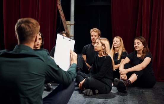 Sitting on the floor. Group of actors in dark colored clothes on rehearsal in the theater photo