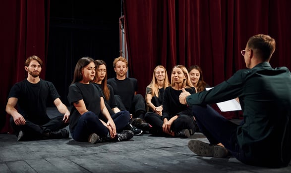Sitting on the floor. Group of actors in dark colored clothes on rehearsal in the theater photo