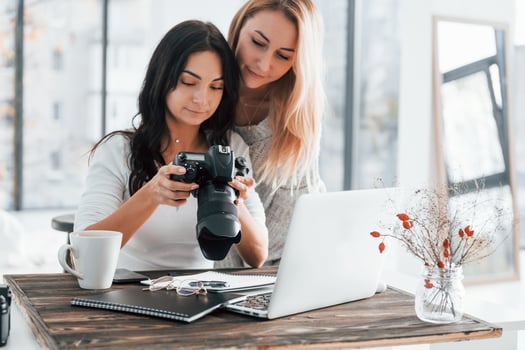 With laptop and camera. Two young female freelancers working indoors in the office at daytime photo