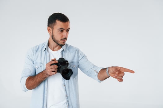 With professional camera. Young handsome man standing indoors against white background photo